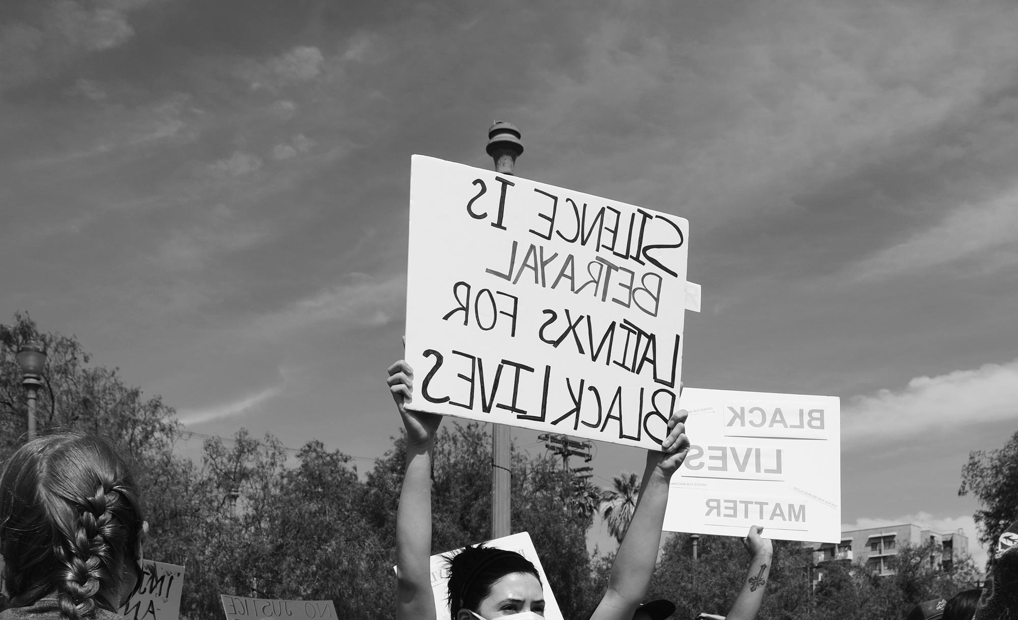 Person holding sign, "Silence is betrayal for Latinx for Black lives"